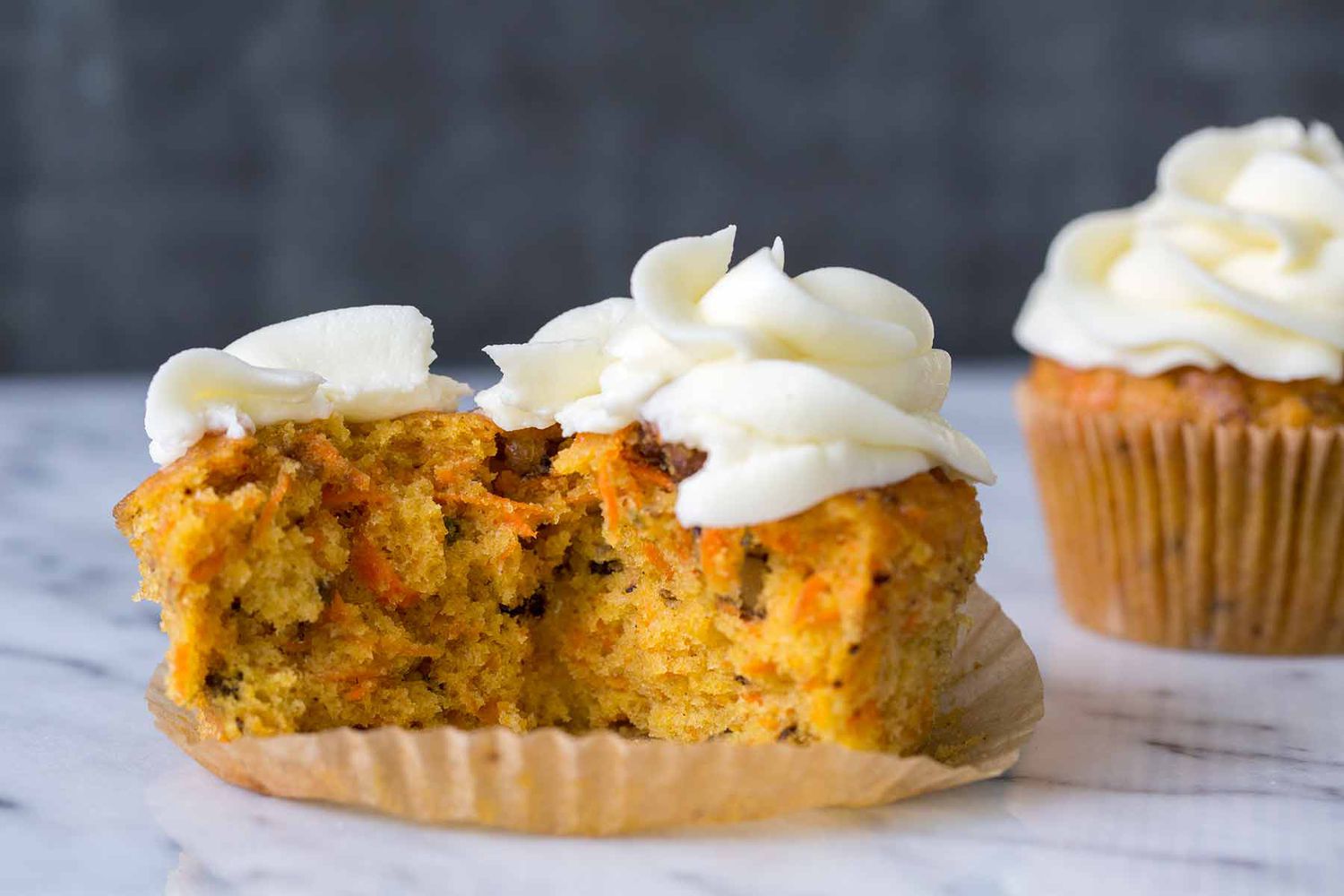 A carrot cake cupcake torn in half, revealing the moist interior of the cake