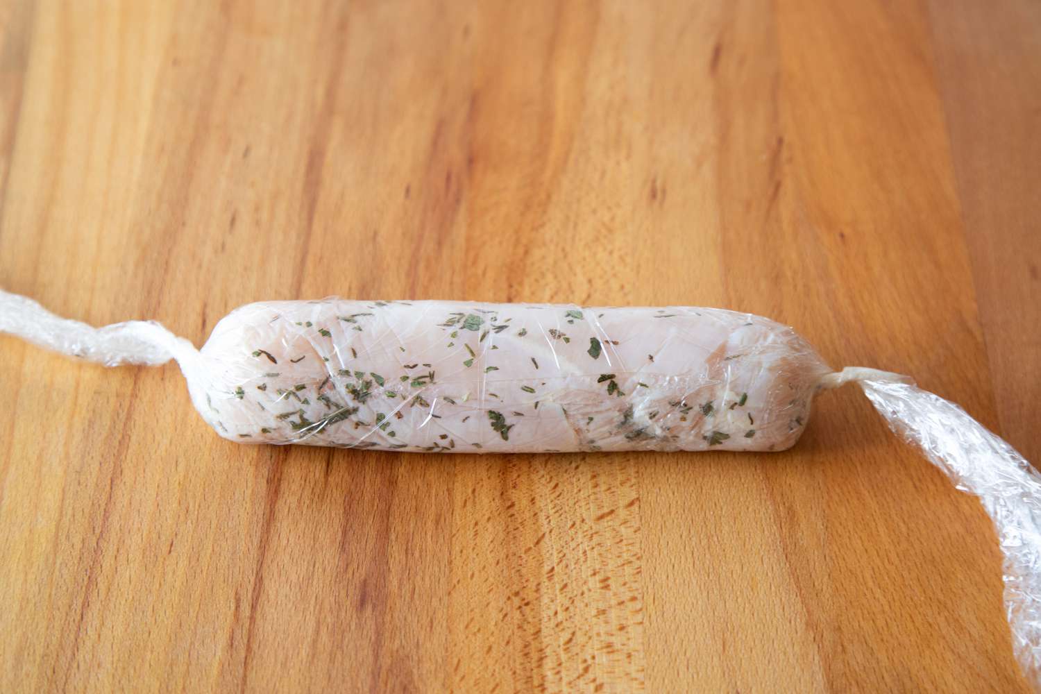 Chicken wrapped in plastic wrap to make a poached chicken recipe.