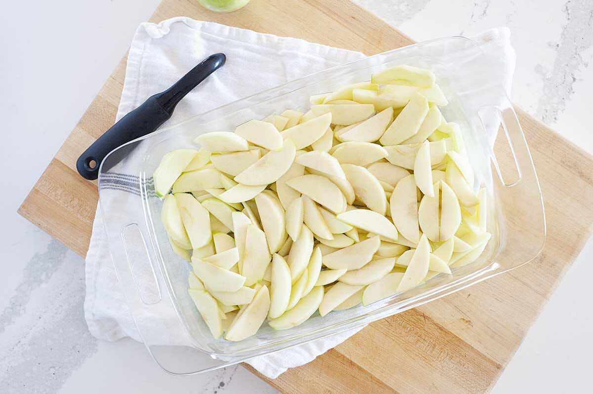 Sliced apples in a glass baking dish for an apple crisp recipe.