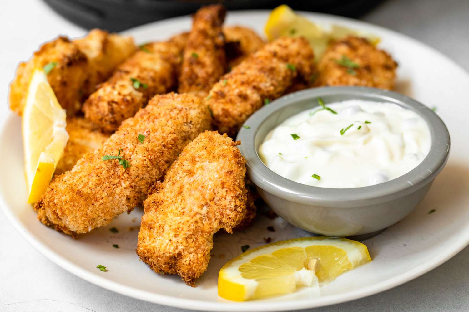 Air Fryer Fish Sticks on a Plate with a Small Bowl of Tartar Sauce and Lemon Slices
