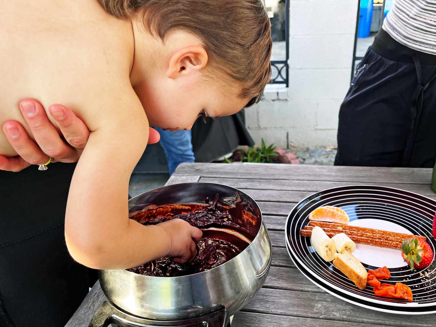 A child dunking their hand in a pot of fondue chocolate