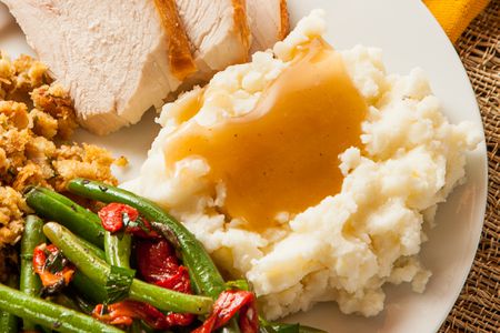 Plate of thanksgiving dinner: slices of turkey, stuffing, green beans and roasted bell peppers, and a mashed potatoes with gravy