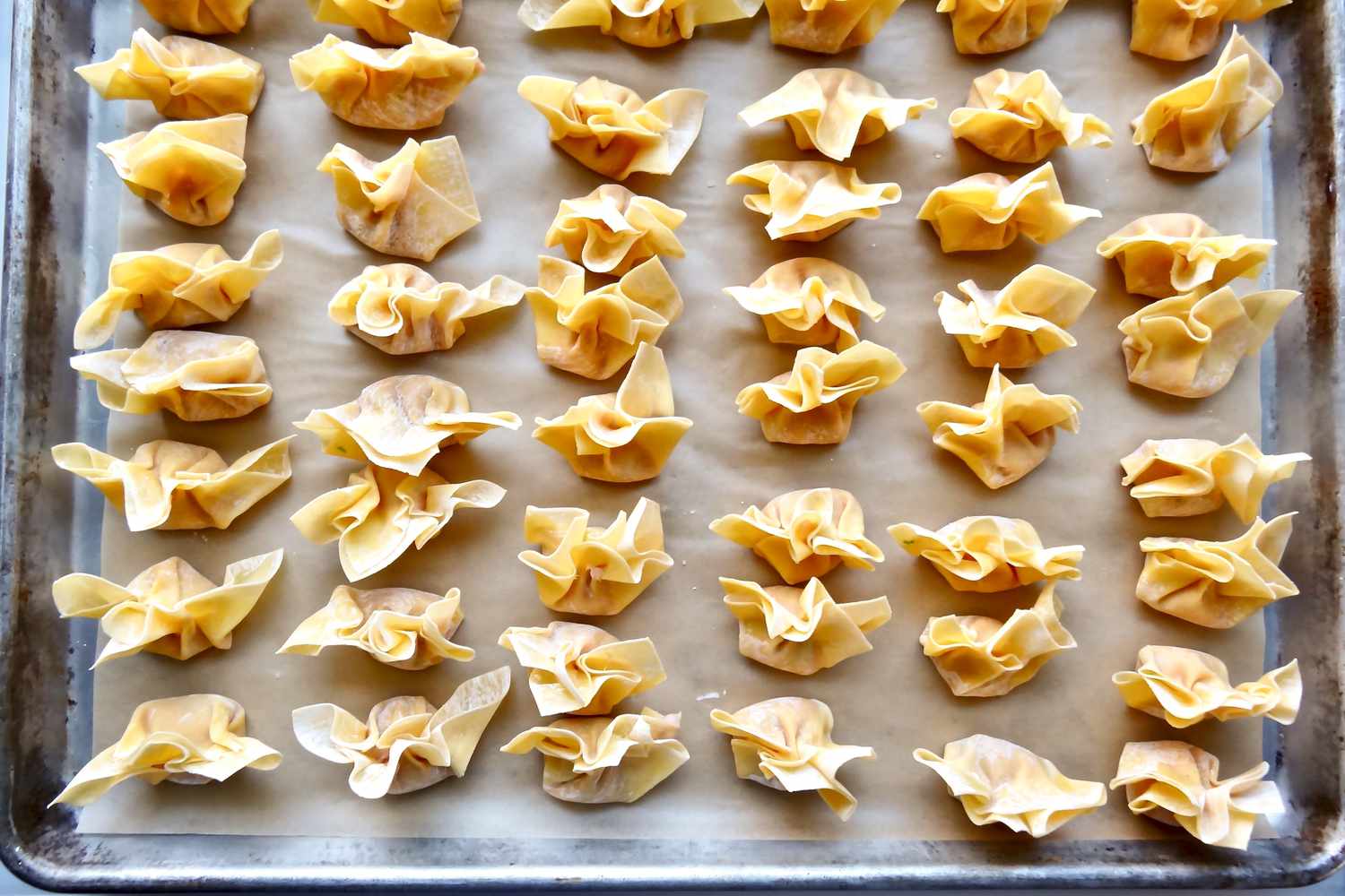 Wontons lined up on a baking sheet for easy pork wontons in homemade chicken broth