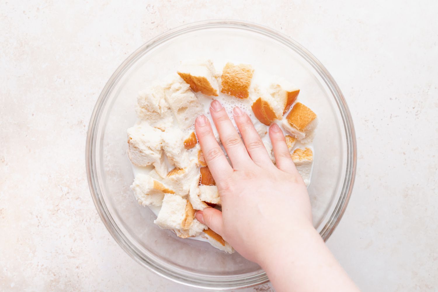 Soaking bread in a milk mixture to make a bread pudding recipe.