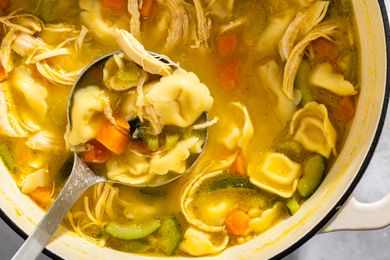 A pot of chicken tortellini soup with vegetables with a ladle scooping a serving