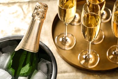 Champagne bottle in an ice bucket next to a tray with filled champagne flutes