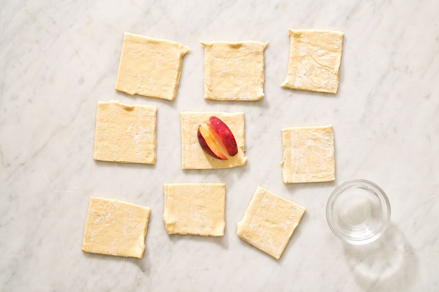 Puff pastry divided into nine squares with two peach slices on one of the squares