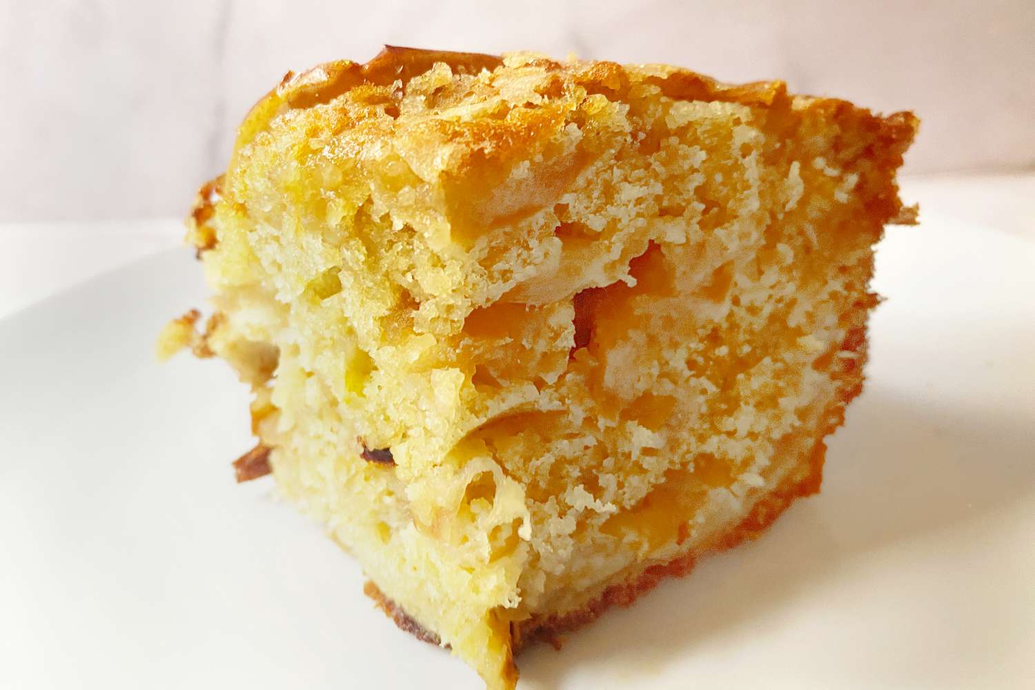 A slice of apple cake on a white plate displaying visible apple pieces in a fluffy texture