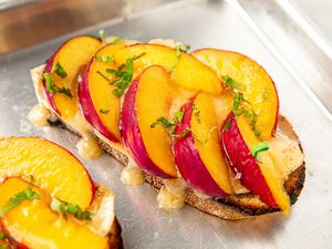 Slices of nectarine and melted brie on toasted bread garnished with fresh herbs