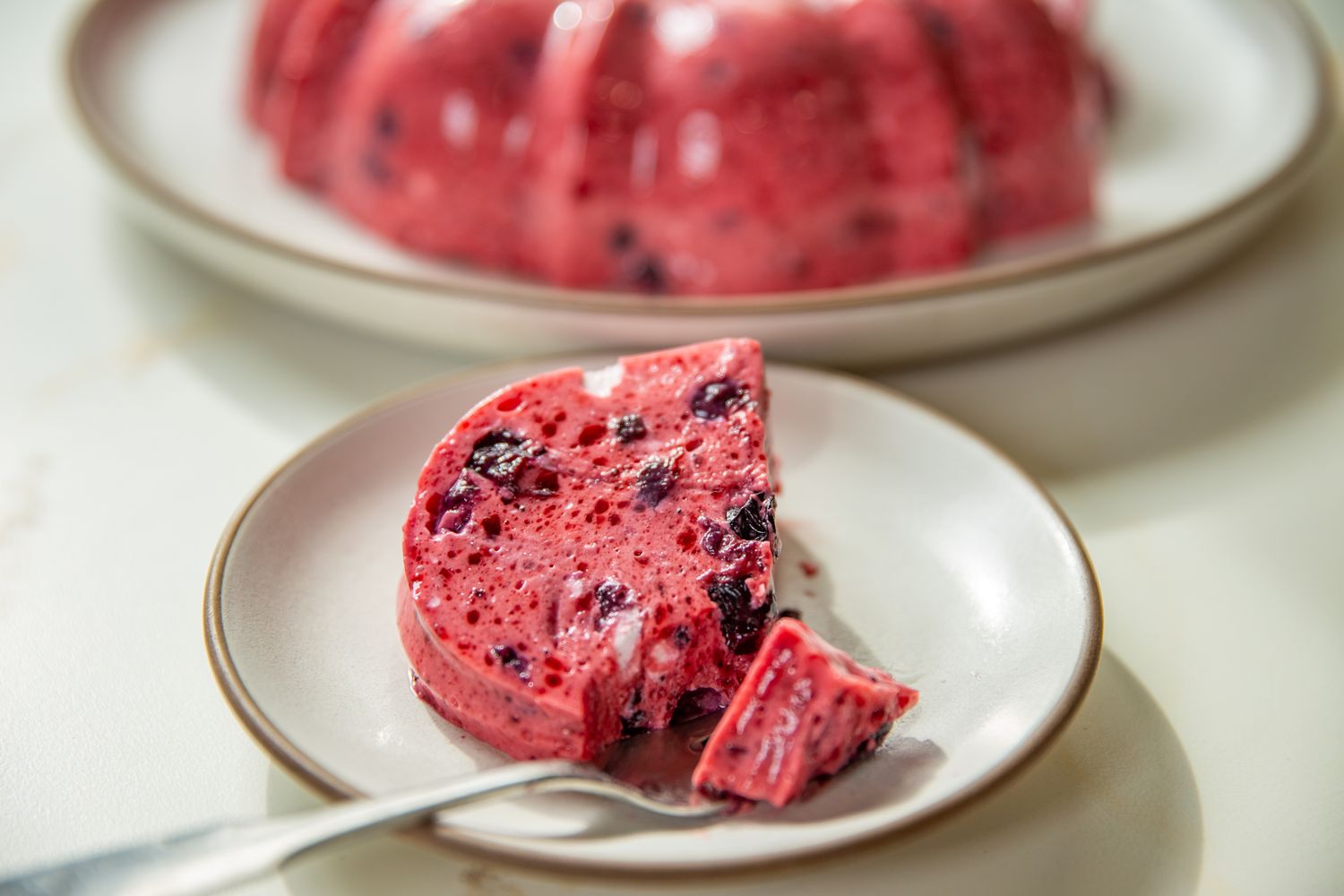 Slice of a blueberry gelatin mold dessert on a plate with a fork mold on a platter in the background