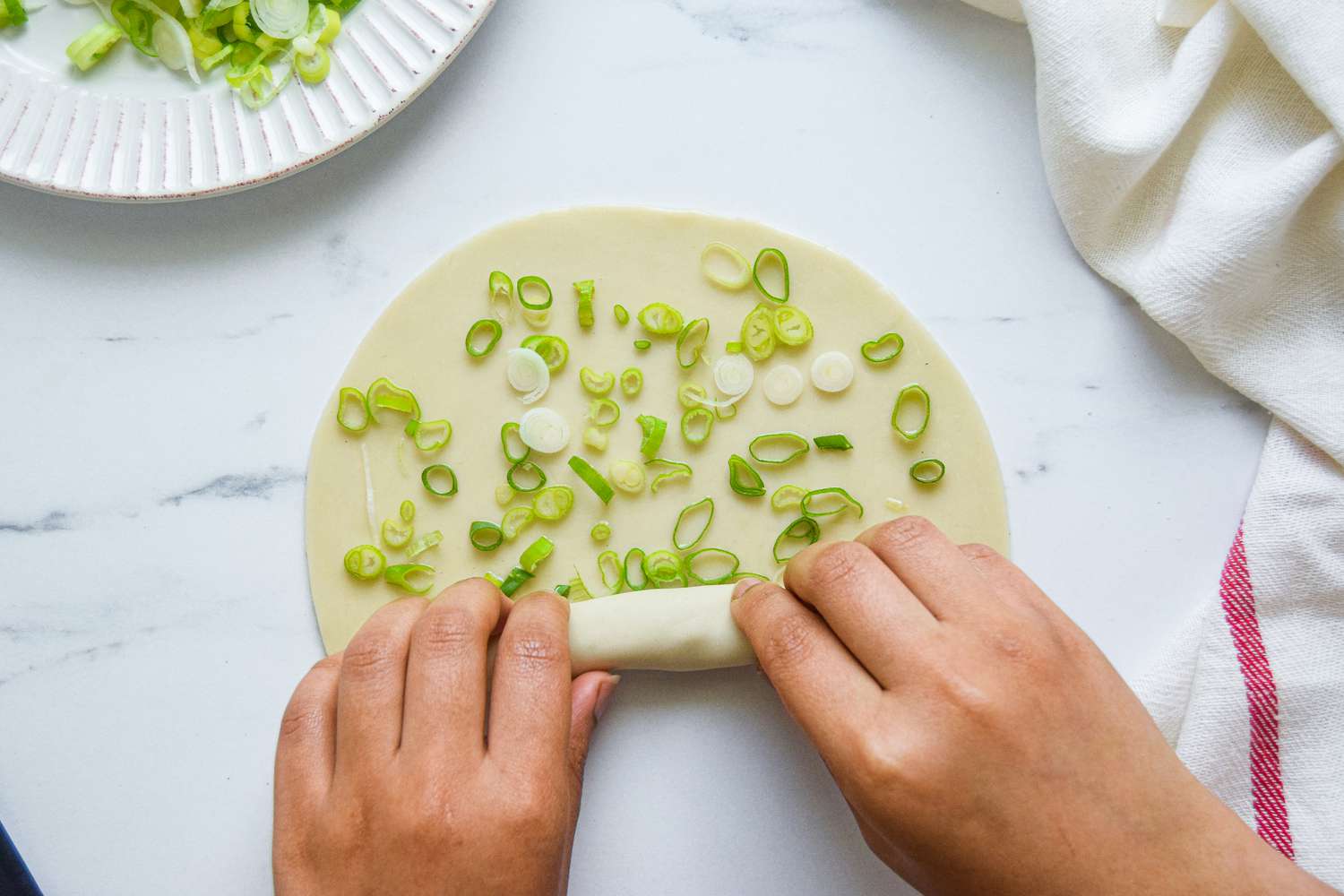 Rolling a homemade scallion pancake with hands.