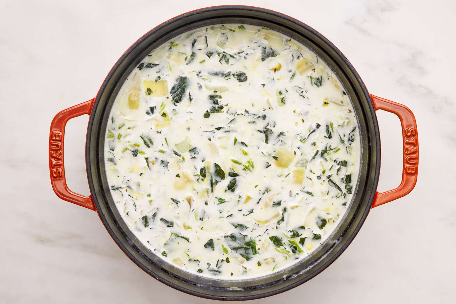 Spinach artichoke dip soup in a Dutch oven after cream cheese and cream mixture stirred into the soup 