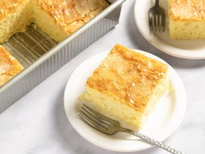 Slices of coca de llanda on plates with forks alongside a baking tray containing more slices