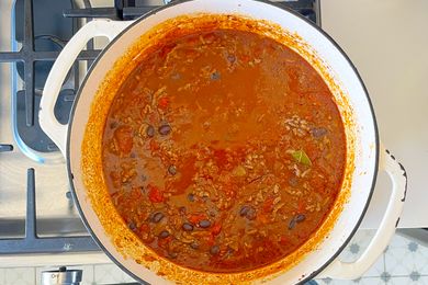 A pot of chili on a stove containing ground meat beans and tomatoes with a visible leafy herb