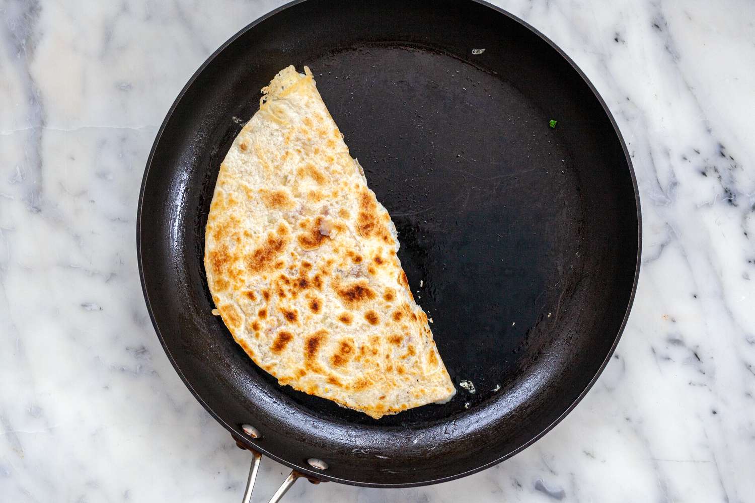 A skillet with a tortilla folded over to show how to make quesadillas.