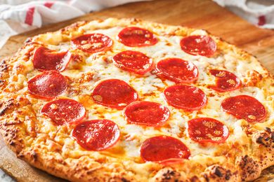 pepperoni pizza on a wooden board surrounded by kitchen towels