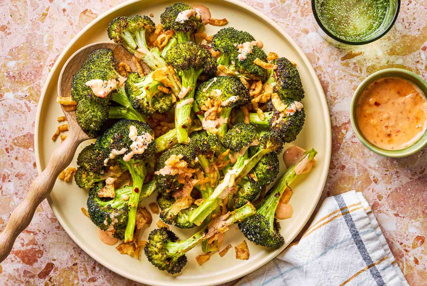 plate of Bang Bang Broccoli smothered with Bang Bang sauce and garnished with fried onions and a small dish of sauce on the side