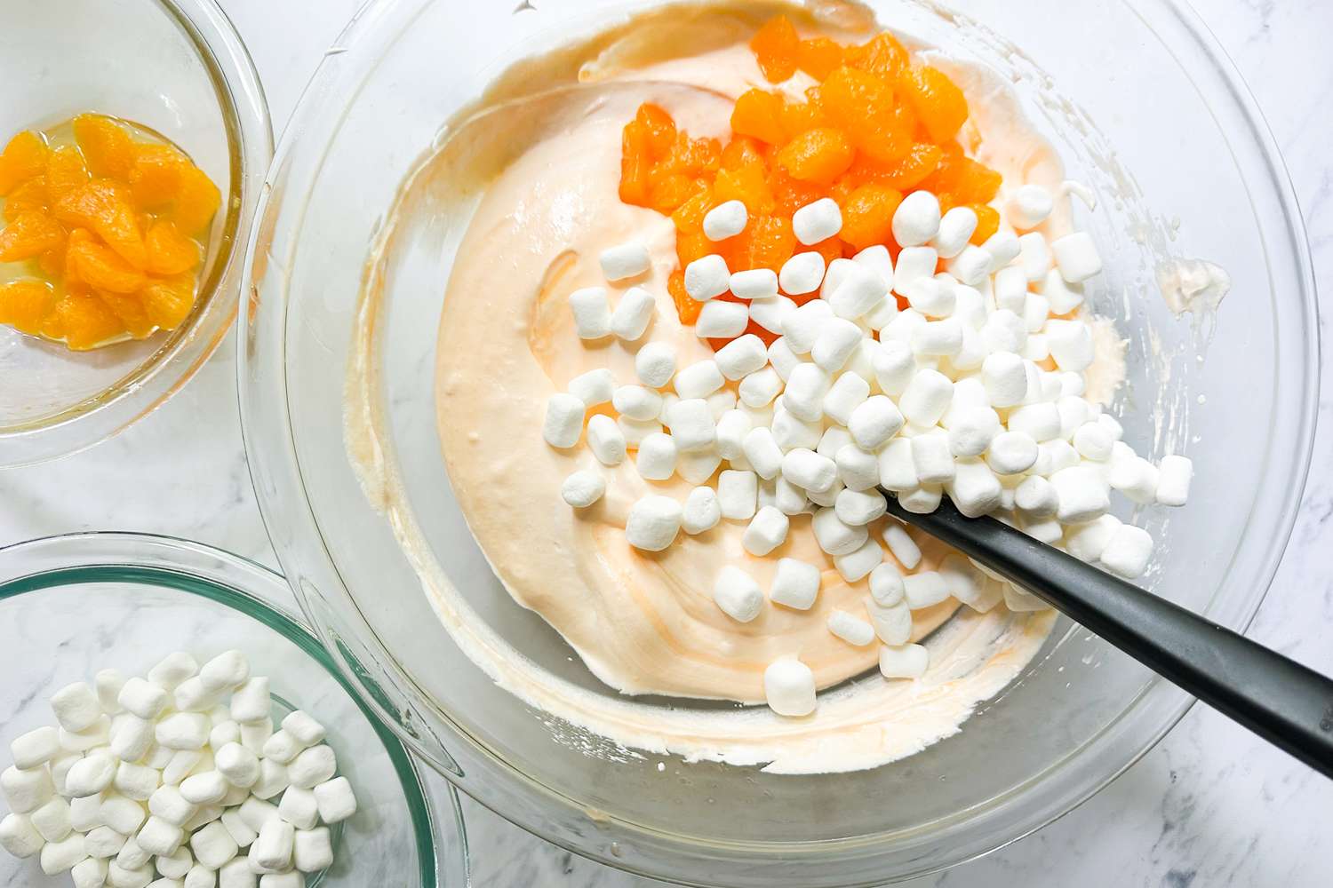 Bowl of orange creamsicle salad with mini marshmallows and orange pieces being mixed