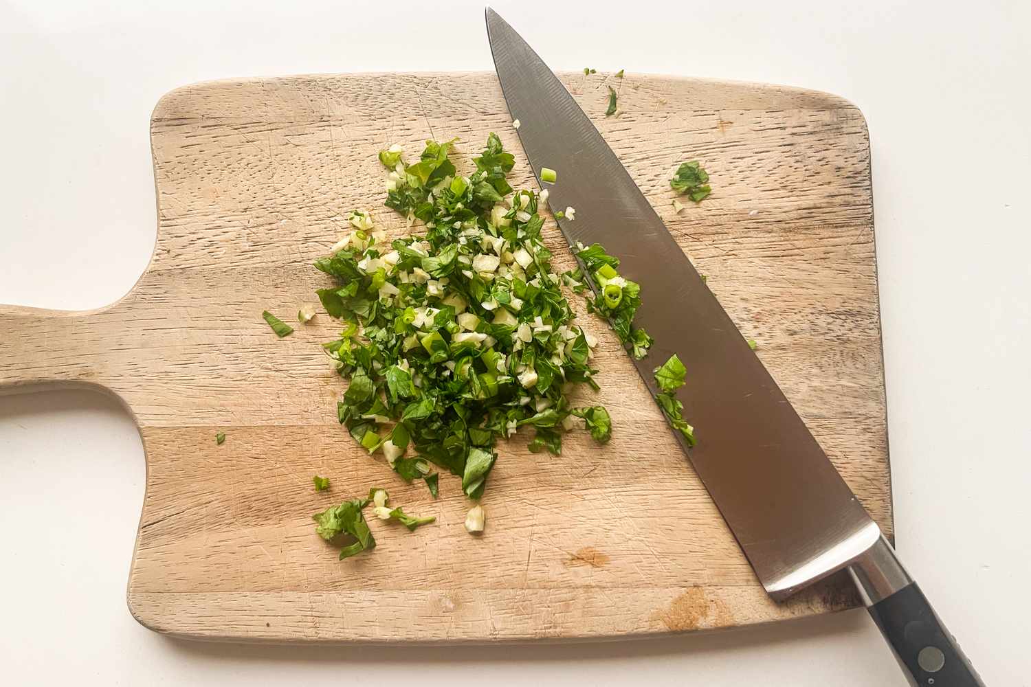 Chopped herbs on a cutting board with a chefs knife
