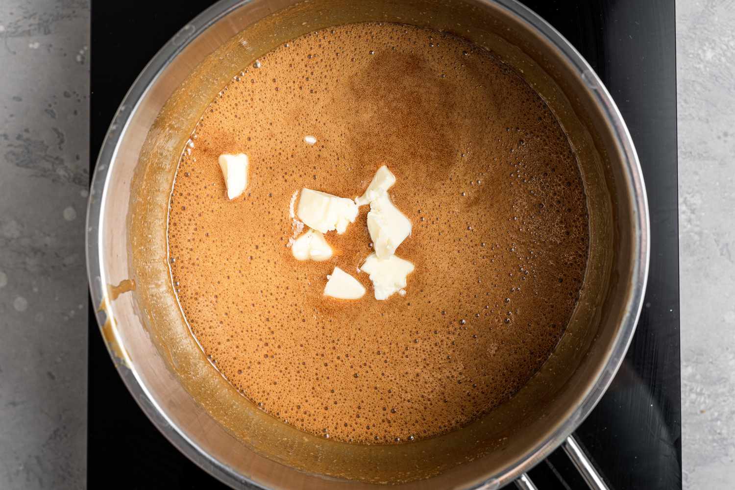 Adding butter to candy mixture to make a pecan praline recipe.