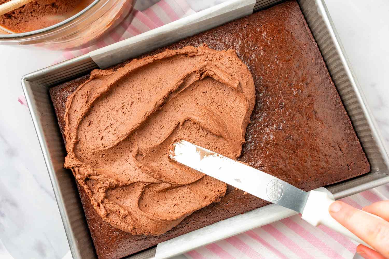 Overhead view of spreading frosting on the baked batter for Never-Fail Chocolate Cake recipe