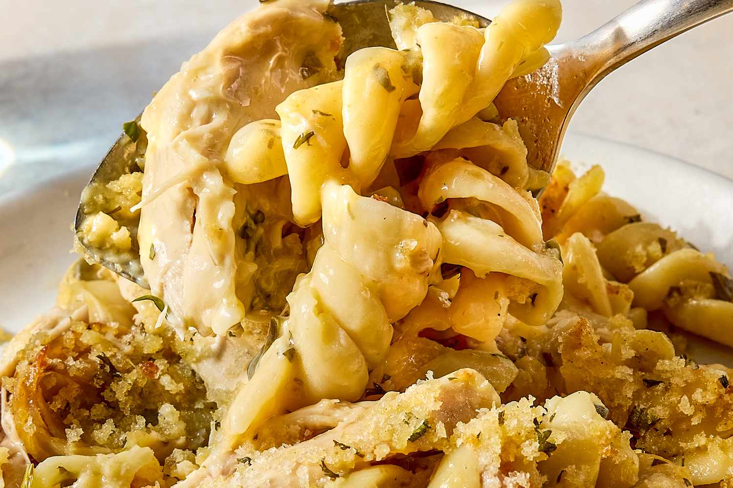 Spoon scooping chicken pasta casserole with noodles and breadcrumbs