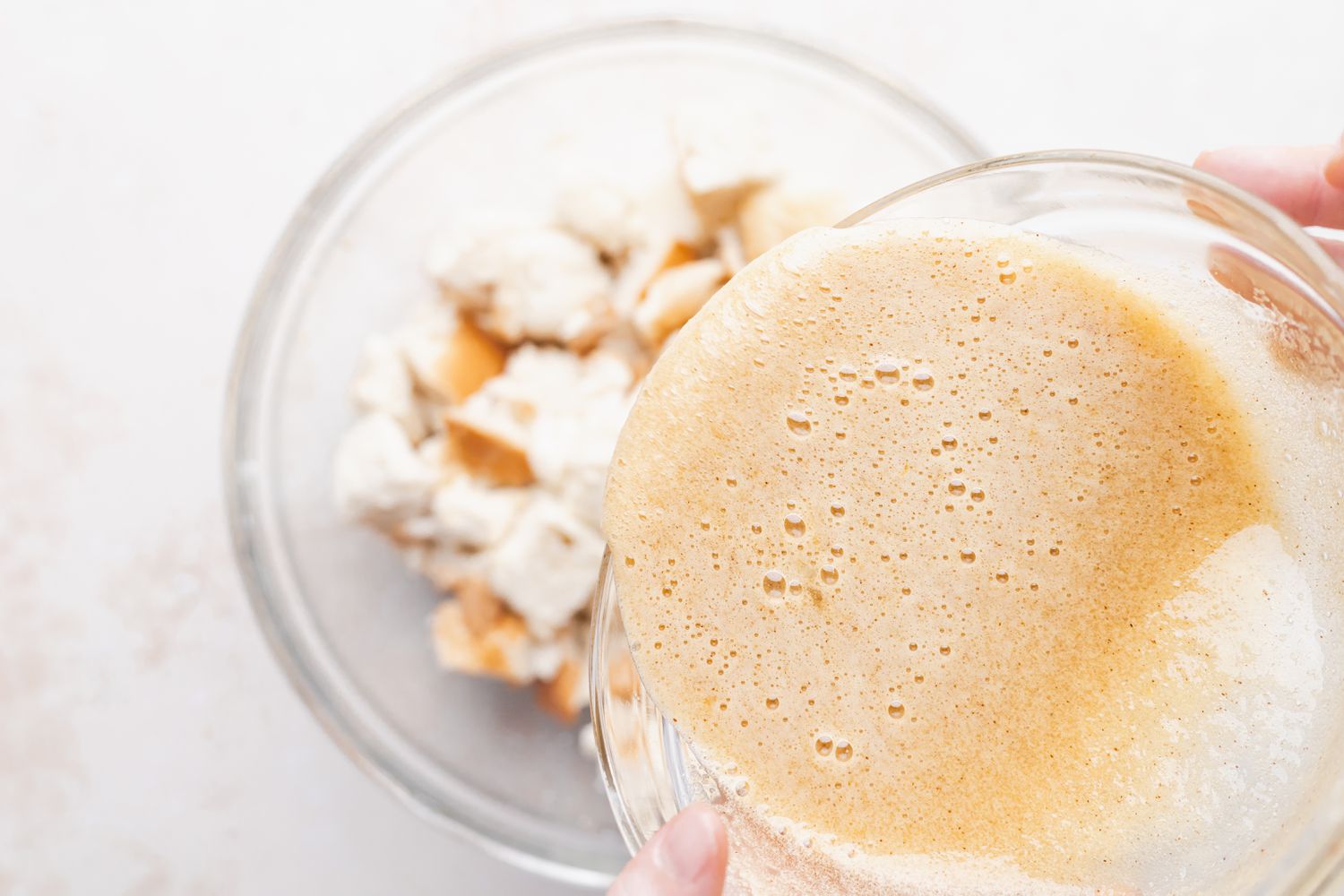 Adding egg mixture to cubed bread for a bread pudding recipe.