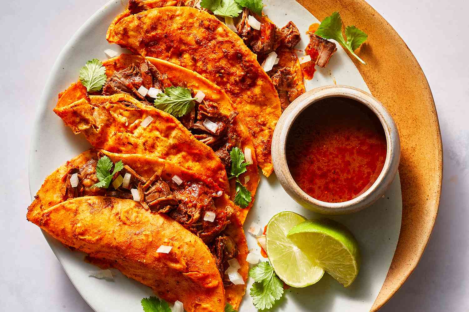 Birria Tacos served with a side of consome and lime wedges 