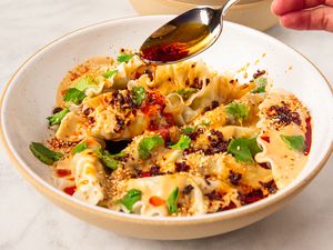 Dumplings on a plate topped with peanut chili sauce and garnished with sesame seeds and herbs with a hand pouring chili oil from a spoon