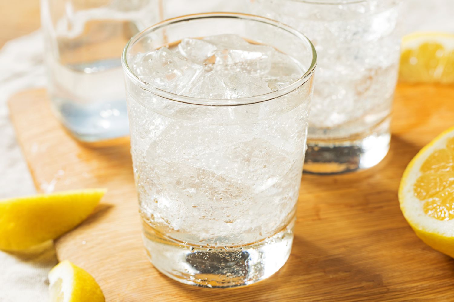 Fizzy water in an ice-filled tumbler with lemon wedges shown cut on a cutting board
