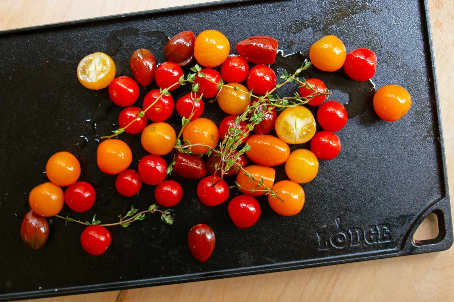 A variety of small whole tomatoes with sprigs of thyme on a black cutting board