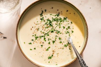 Bowl of cauliflower bisque garnished with chopped herbs and black pepper with a spoon placed inside