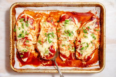 Overhead view of a baking sheet of four bbq baked chicken breasts topped with cheese and green onions on parchment paper