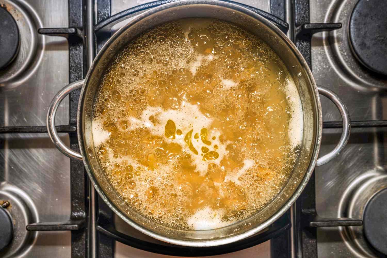 Overhead shot of a metal cooking pan with boiling water and wholewheat penne pasta on a stove