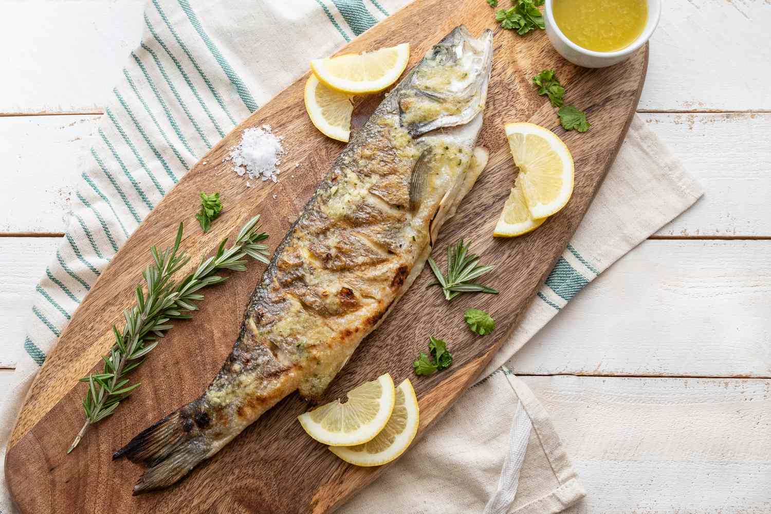 Overhead view of a whole branzino on a platter with lemon wedges and herbs.