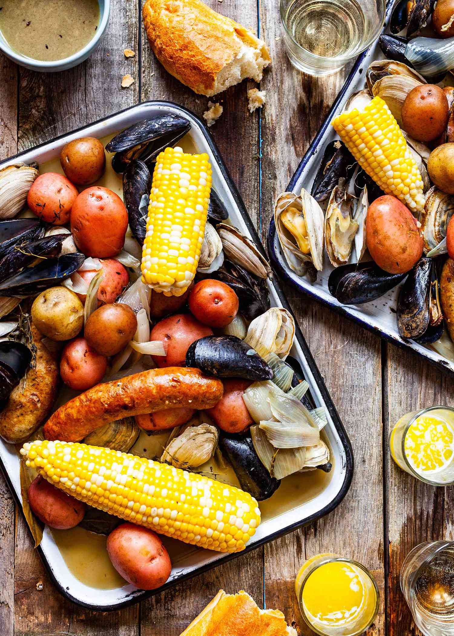 Platters of clam bake with corn on the cob, sausages, clams, potatoes, melted butter