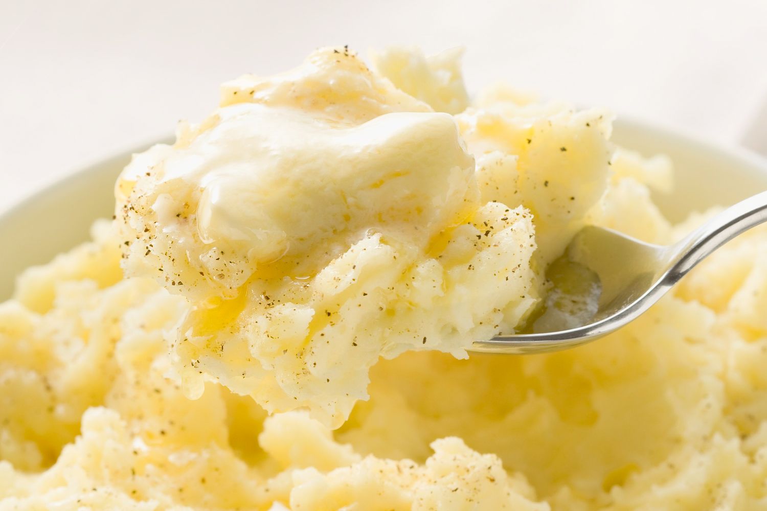 A fork holding a portion of mashed potatoes with butter on a plate