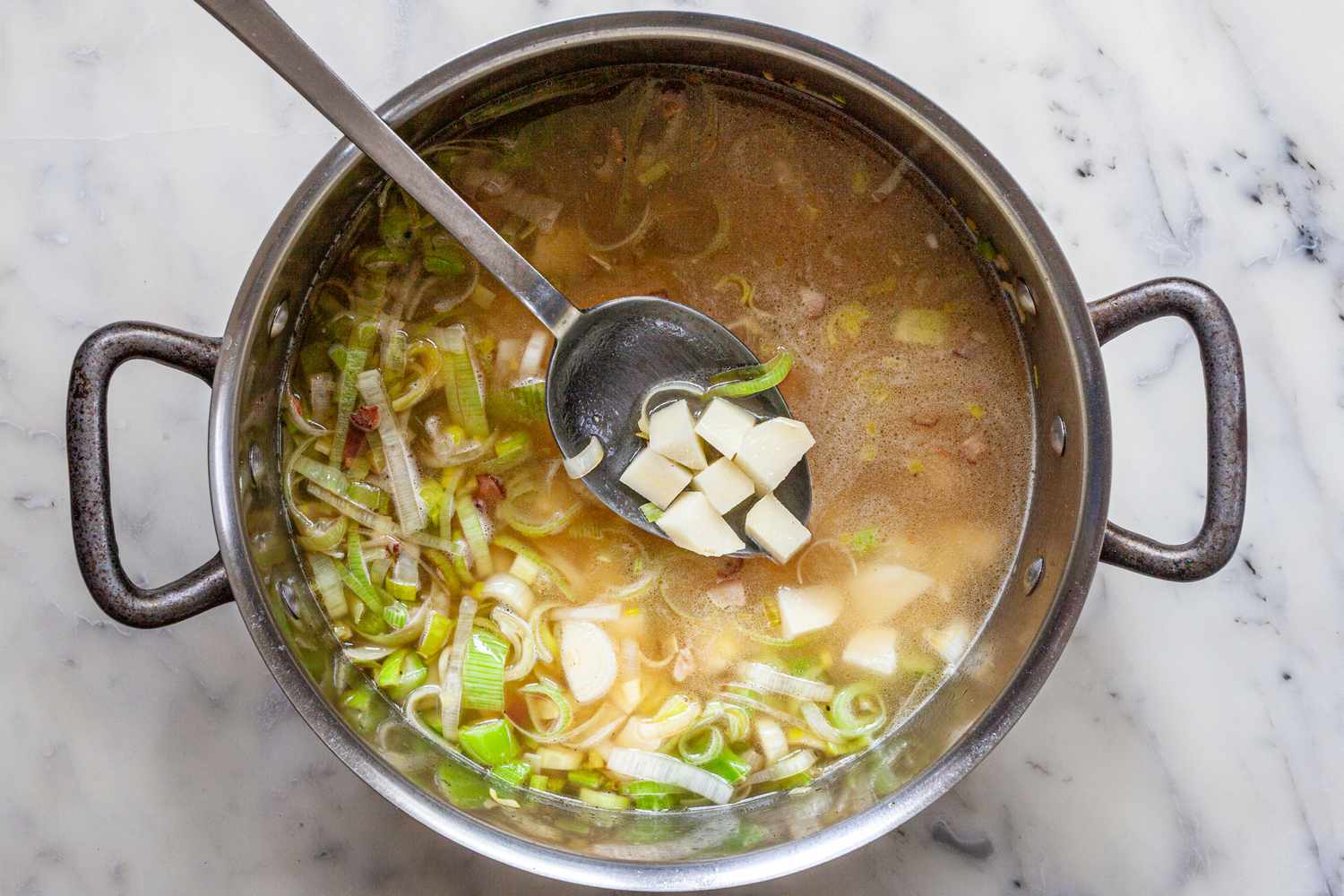 Potatoes and Chicken Stock Stirred into the Pot with a Few Potato Pieces Lifted up Using a Spoon for Crab Chowder Recipe