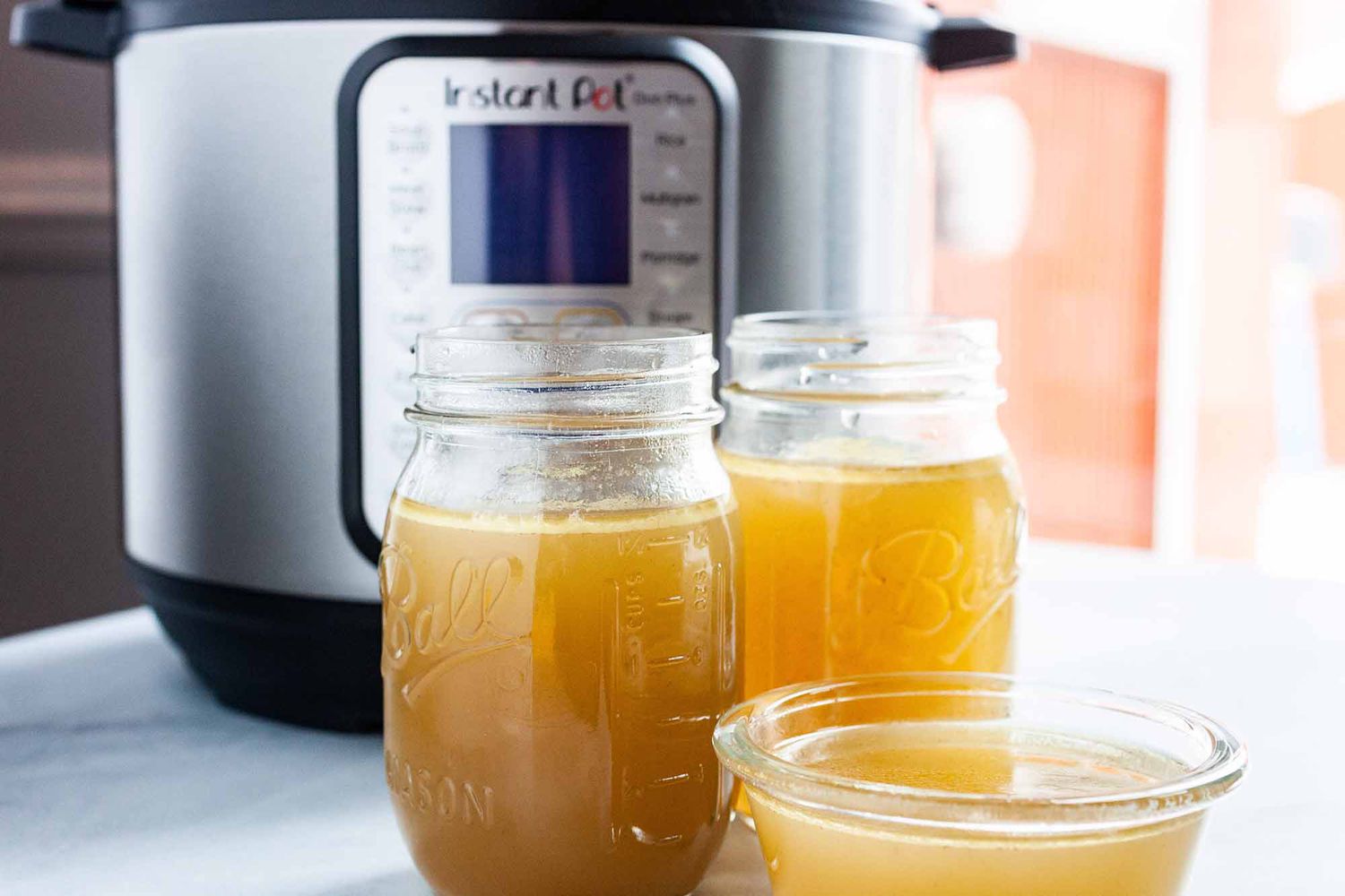 How to Make Chicken Stock in the Instant Pot - - two ball jars filled with chicken sock with an instant pot pressure cooker behind them