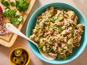 A bowl of tuna and avocado salad with a spoon jalapeos and chopped herbs nearby