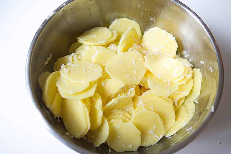 tossing potatoes with gruyere for cheesy scalloped potatoes