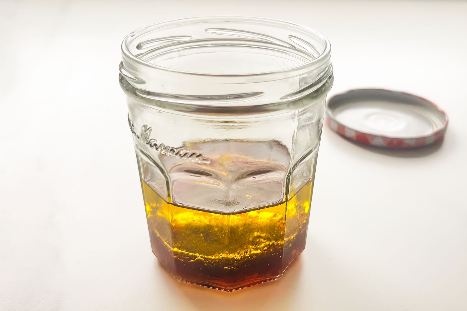 A glass jar containing layered salad dressing ingredients with the lid off and placed nearby