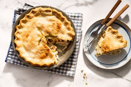 Moravian chicken pie on a plate and in a dish with a missing slice utensils placed beside on a checkered cloth on a marble surface