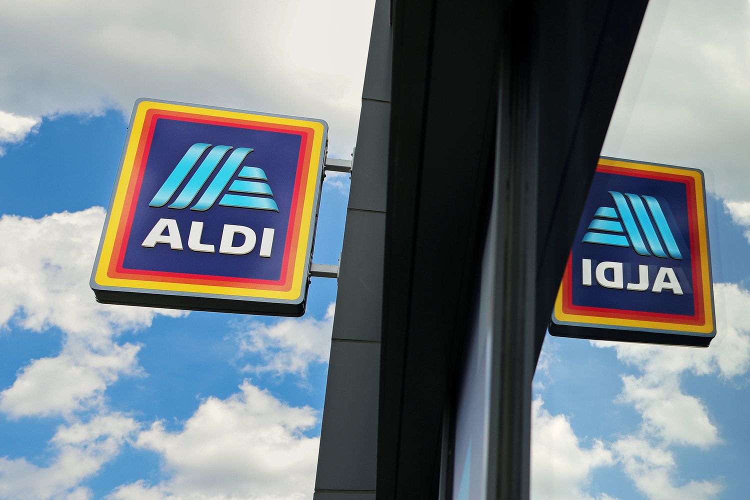 Aldi store signage reflecting on glass, against a background of clouds