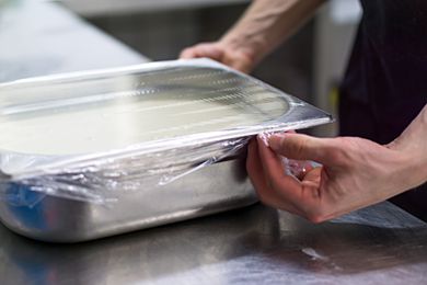 A cook stretching plastic wrap over a hotel pan in a restaurant kitchen