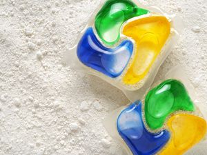 Close up of two multicolored dishwasher detergent pods on a background of dish detergent powder