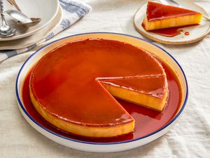 Plate of flan at a table setting with a serving on a plate and a stack of plates with utensils 