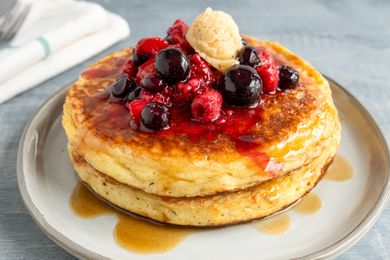 Pancakes topped with mixed berries syrup and a dollop of butter on a plate