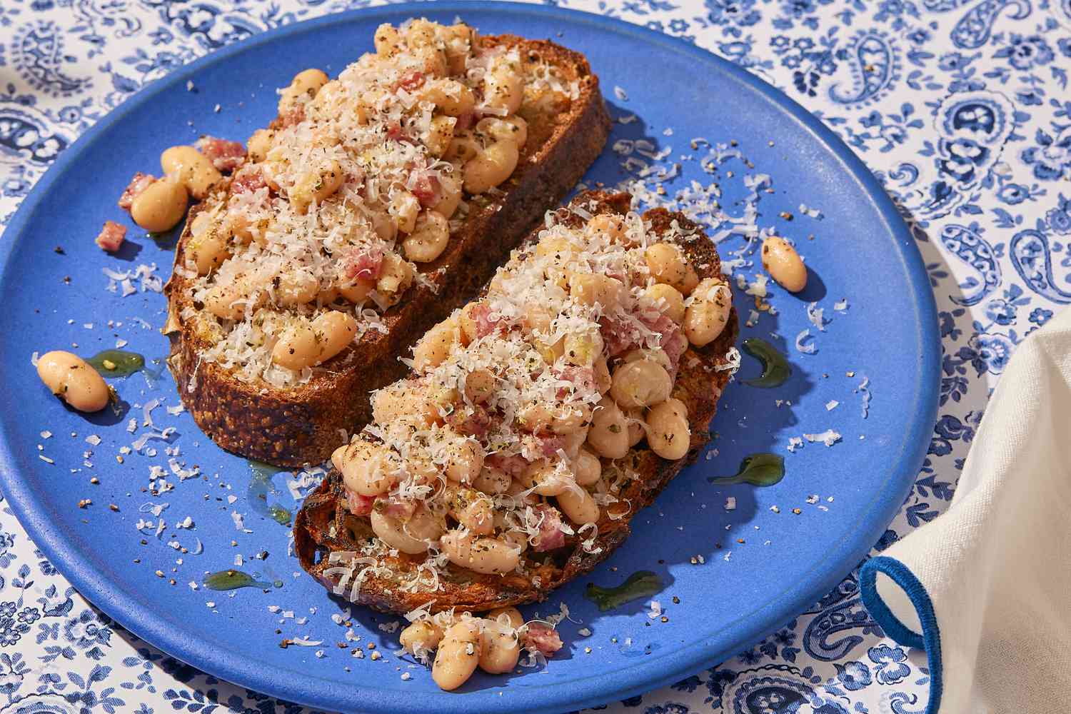 Angled view of a blue plate of two pieces of White Bean and Salami Toasts on a paisley tablecloth