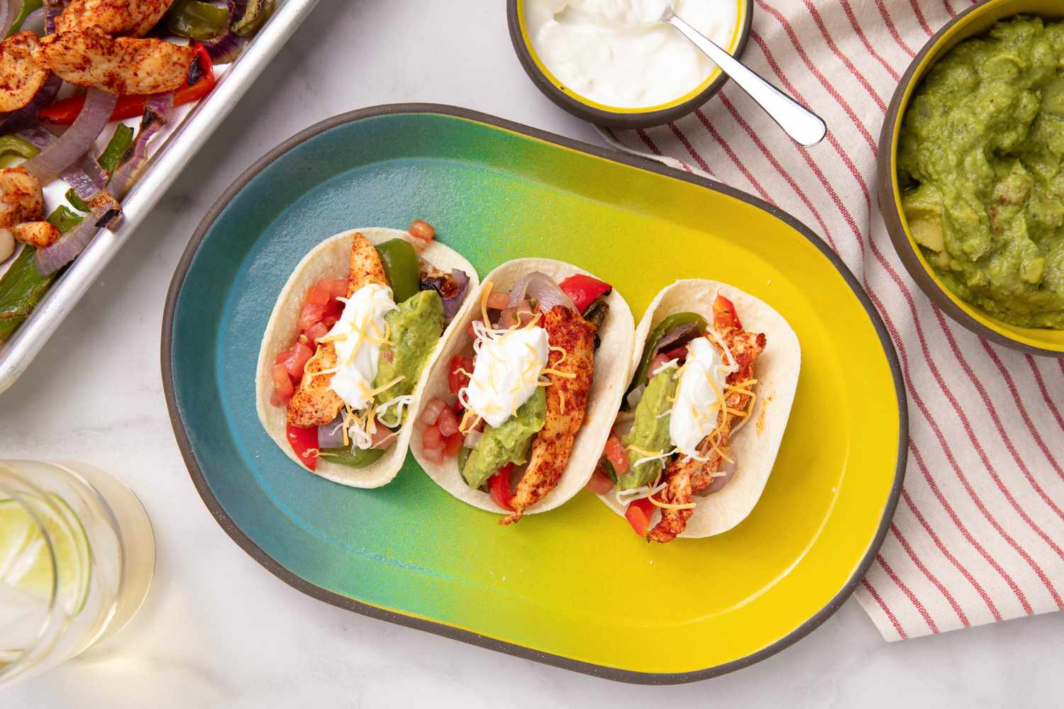 Three tacos with chicken vegetables sour cream and guacamole on a plate surrounded by salsa and toppings